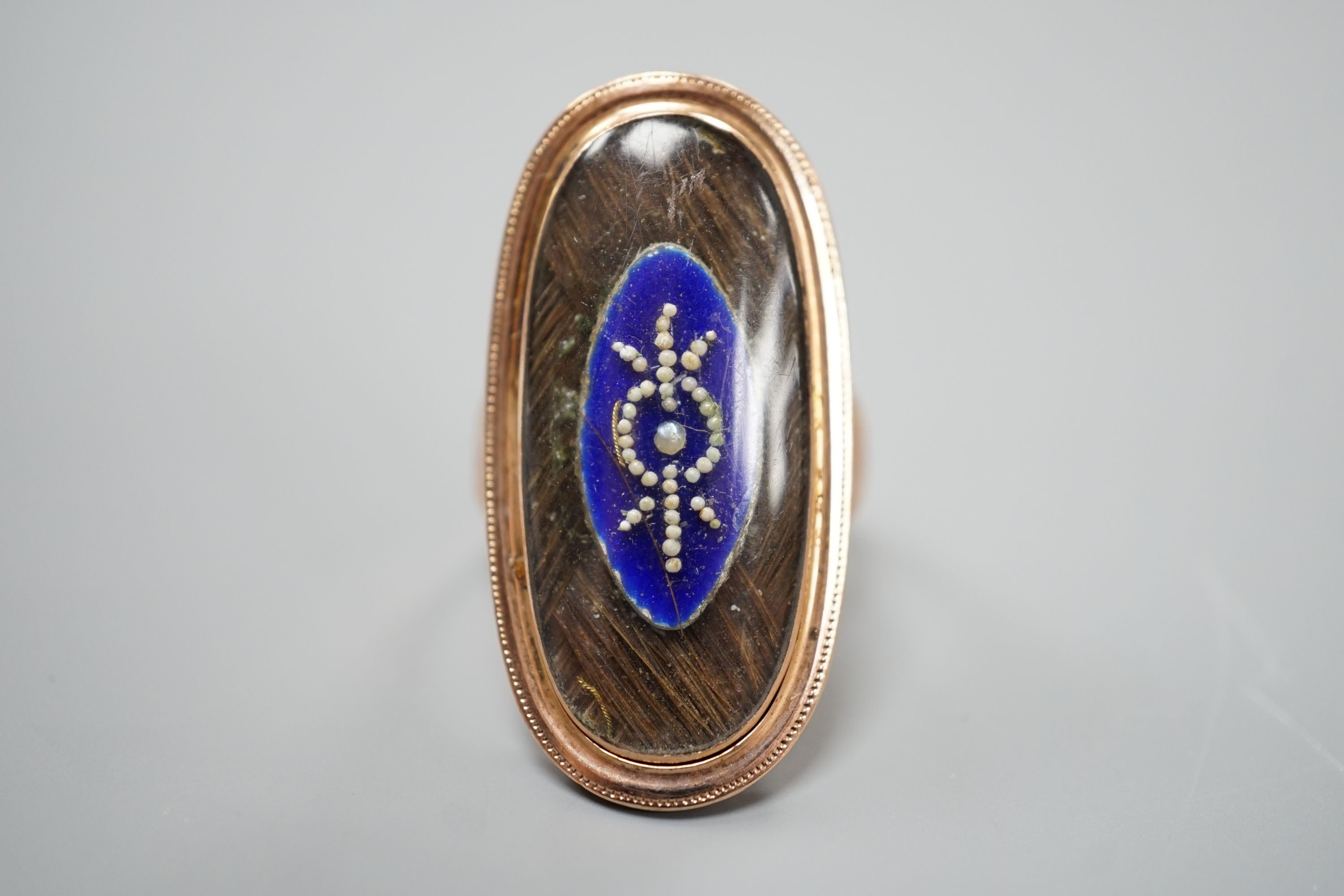 A 19th century yellow metal, blue enamel, seed pearl and plaited hair set oval mourning ring, size M, gross weight 7.2 grams.